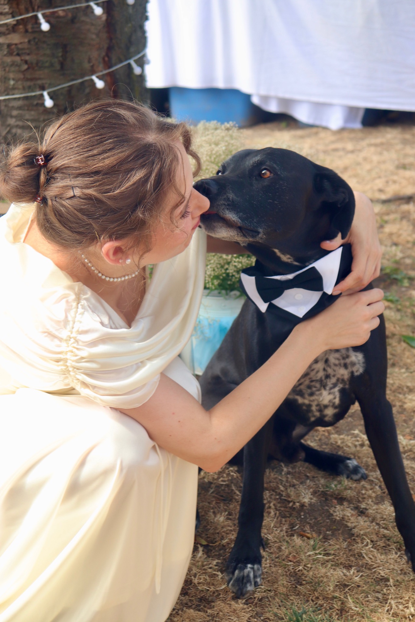 Vanessa cuddling a black dog wearing a bow tie