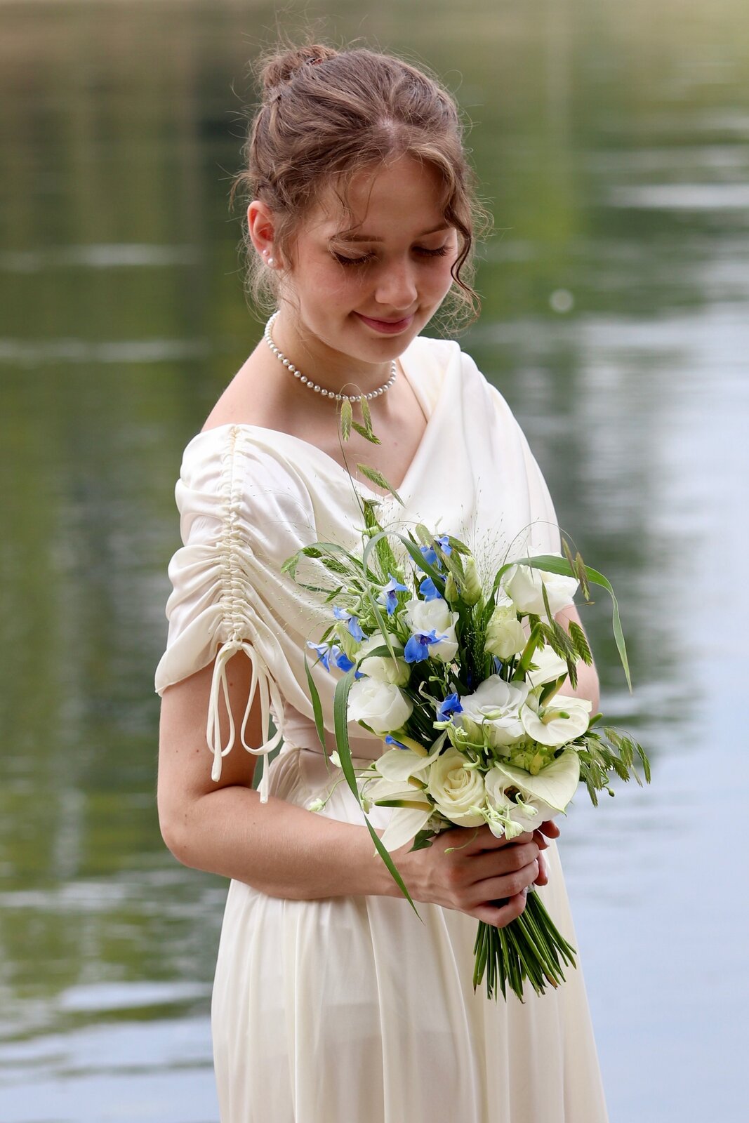 Vanessa looking down at her bouquet beside the water